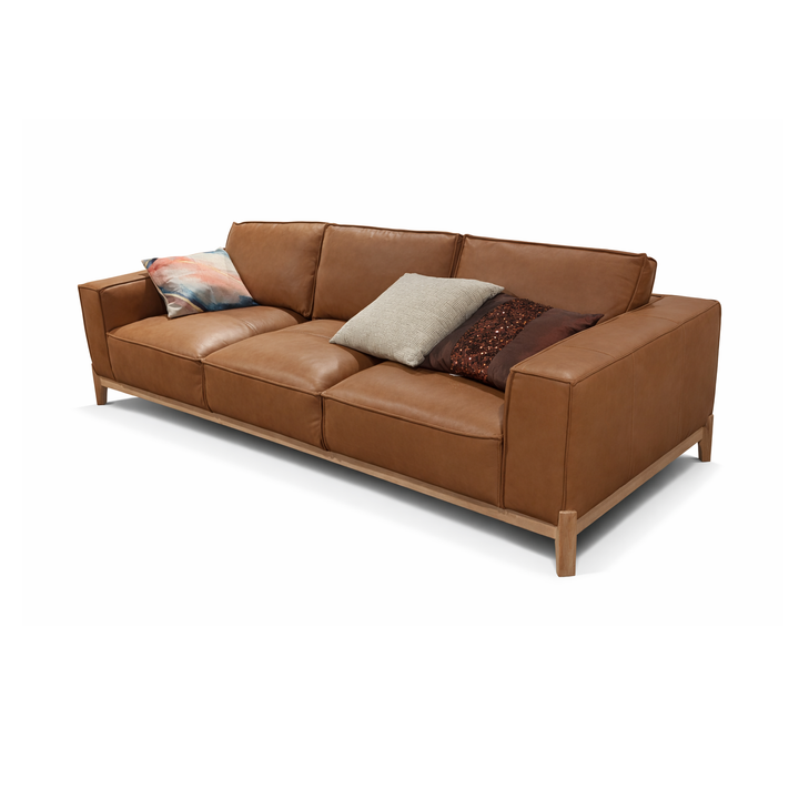 Cognac leather sofa with tapered wooden legs and three throw pillows in beige, brown, and abstract patterns.