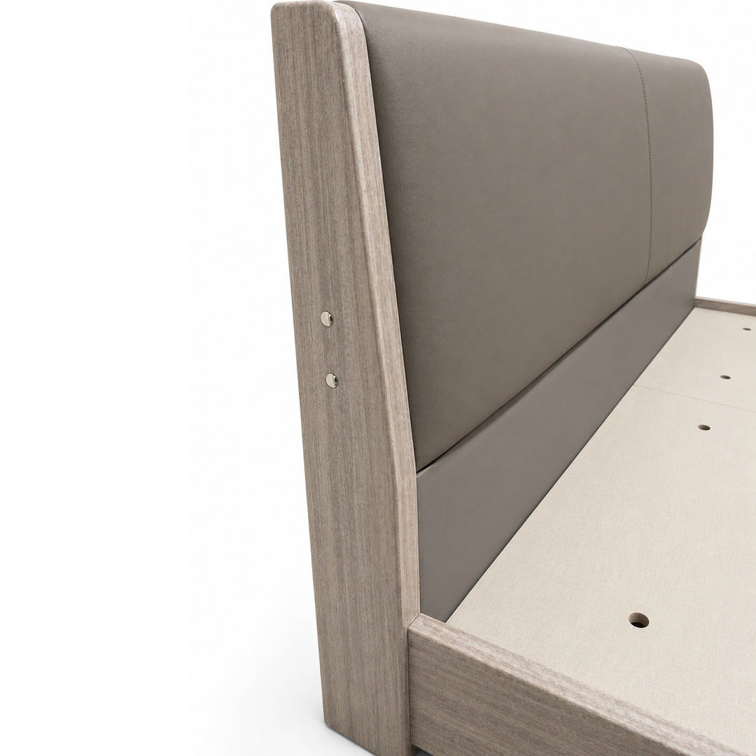 Close-up of a grey upholstered headboard on a light wood frame, showing side screws and bed base with slat holes.