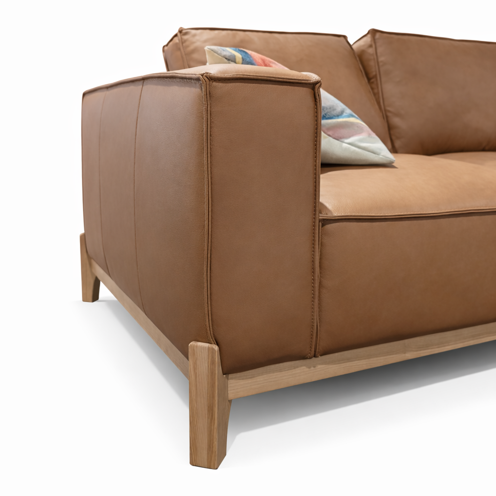 Cognac leather sofa with light wood legs and base, featuring plush cushions and throw pillows.