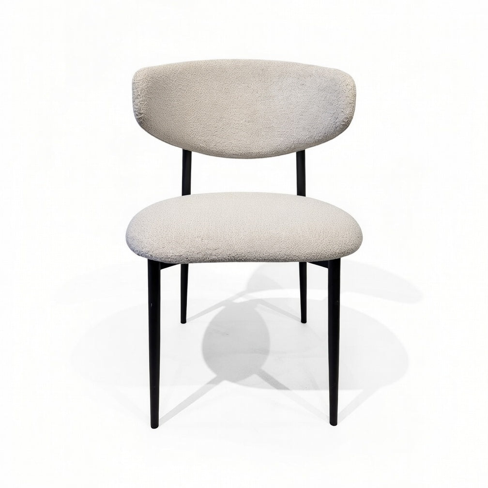 Cream upholstered dining chair with a rounded backrest and slender black metal legs.