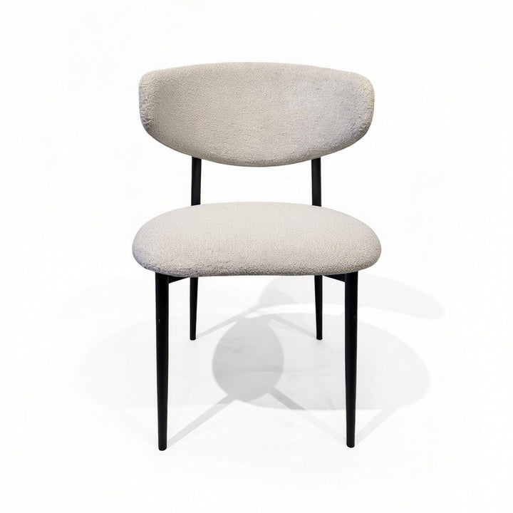 Cream upholstered dining chair with a rounded backrest and slender black metal legs.