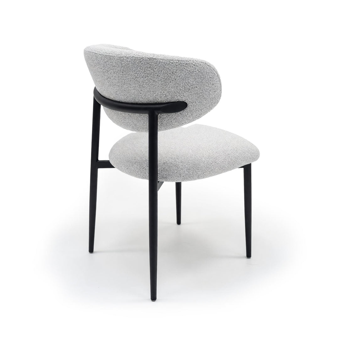 Rear view of a dining chair with light grey textured upholstery and slender black metal legs.