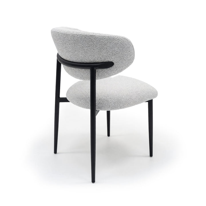 Rear view of a dining chair with light grey textured upholstery and slender black metal legs.