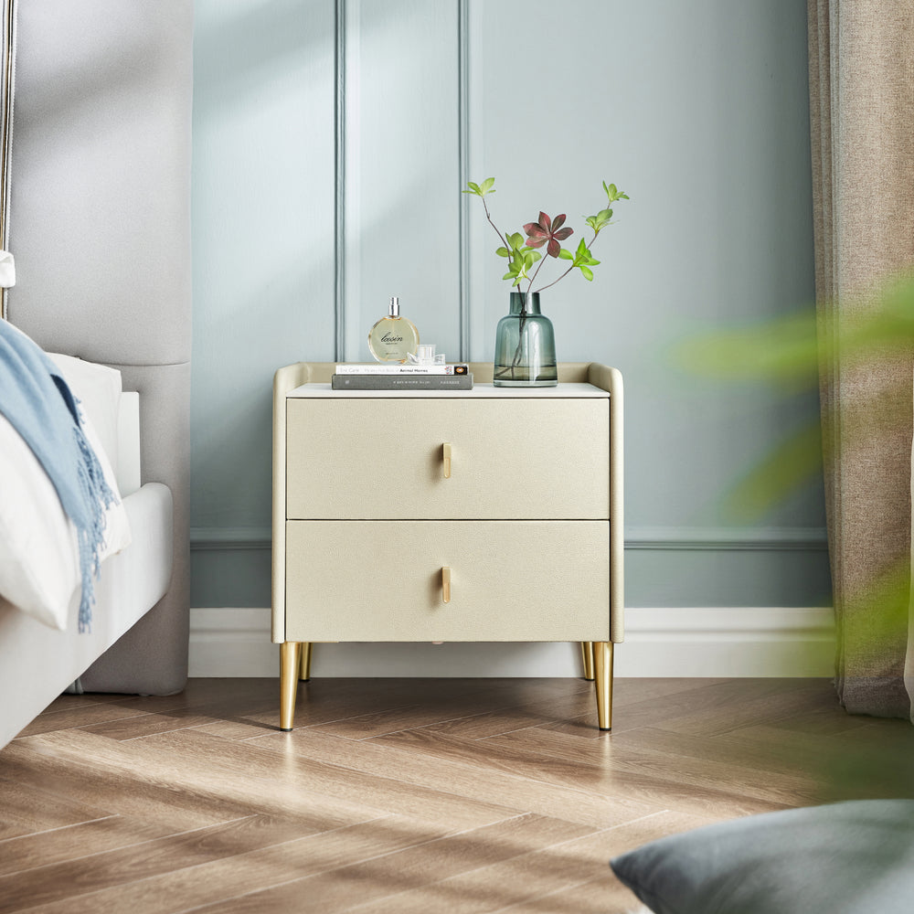 LISA Two Drawer nightstand in textured cream with gold tapered legs and brass handles, styled with a perfume and vase.