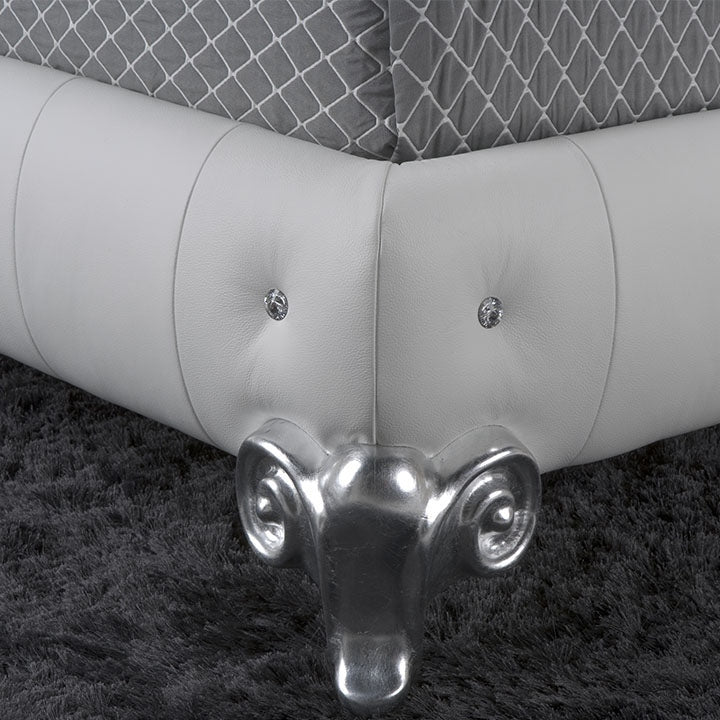 Close-up of a white leather bed frame with crystal button accents and silver ram's head-shaped legs on a grey carpet.