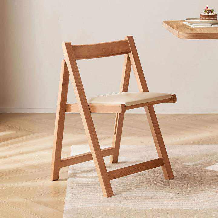 Natural wood folding chair with a cream upholstered seat and minimalist design.