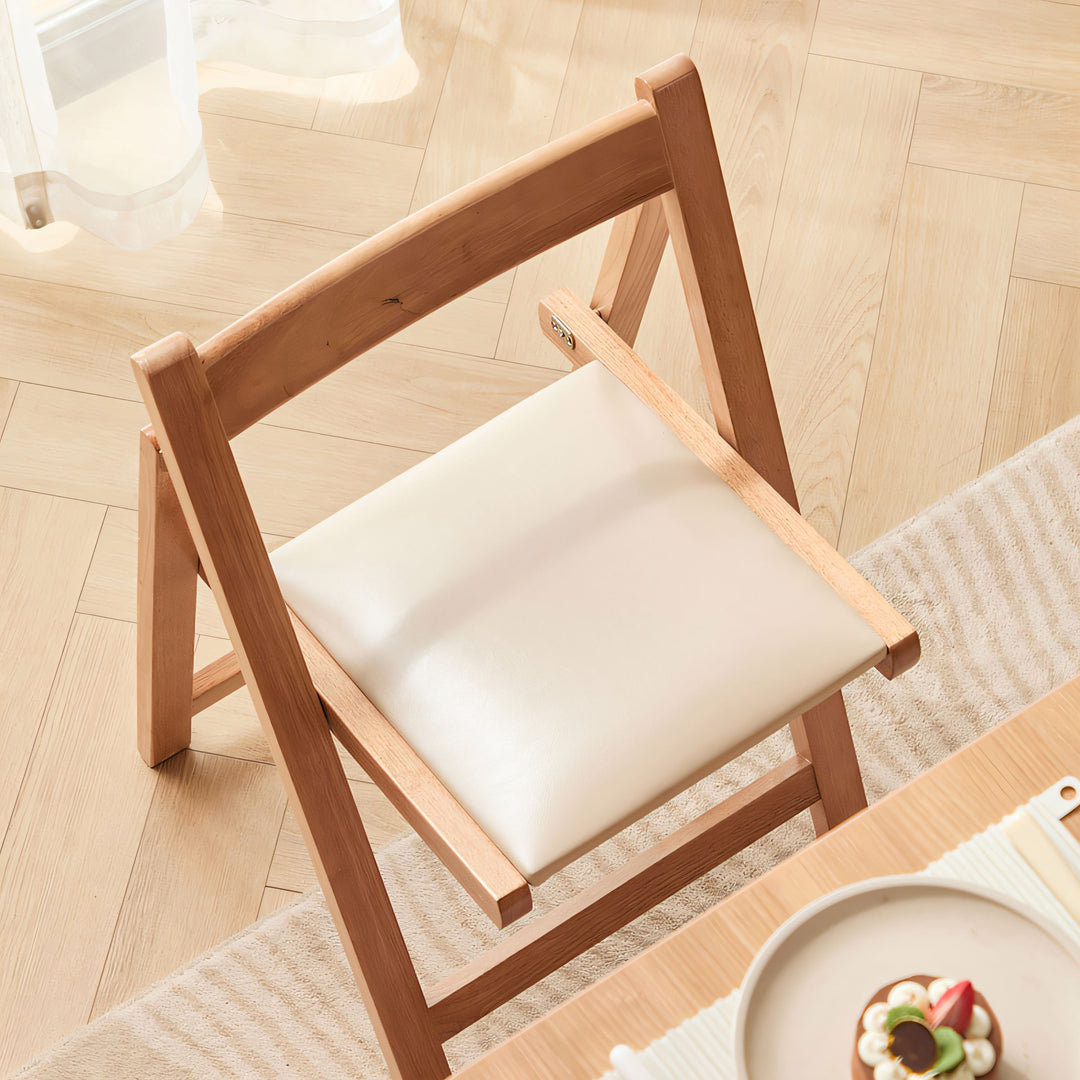 Foldable chair with a natural light wood frame and a cream leather seat, positioned on a light wooden floor.