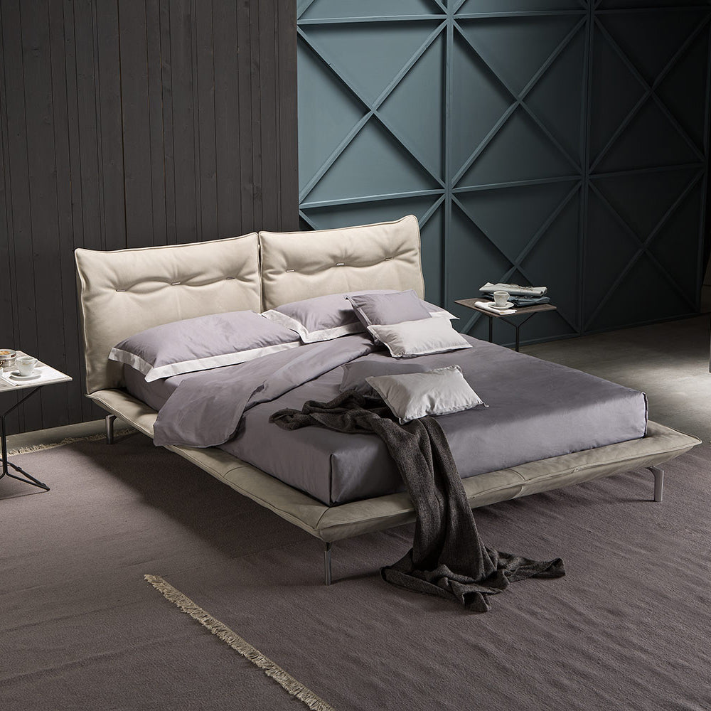 Cream upholstered platform bed featuring a tufted double headboard, styled with lavender linens and a dark throw blanket.