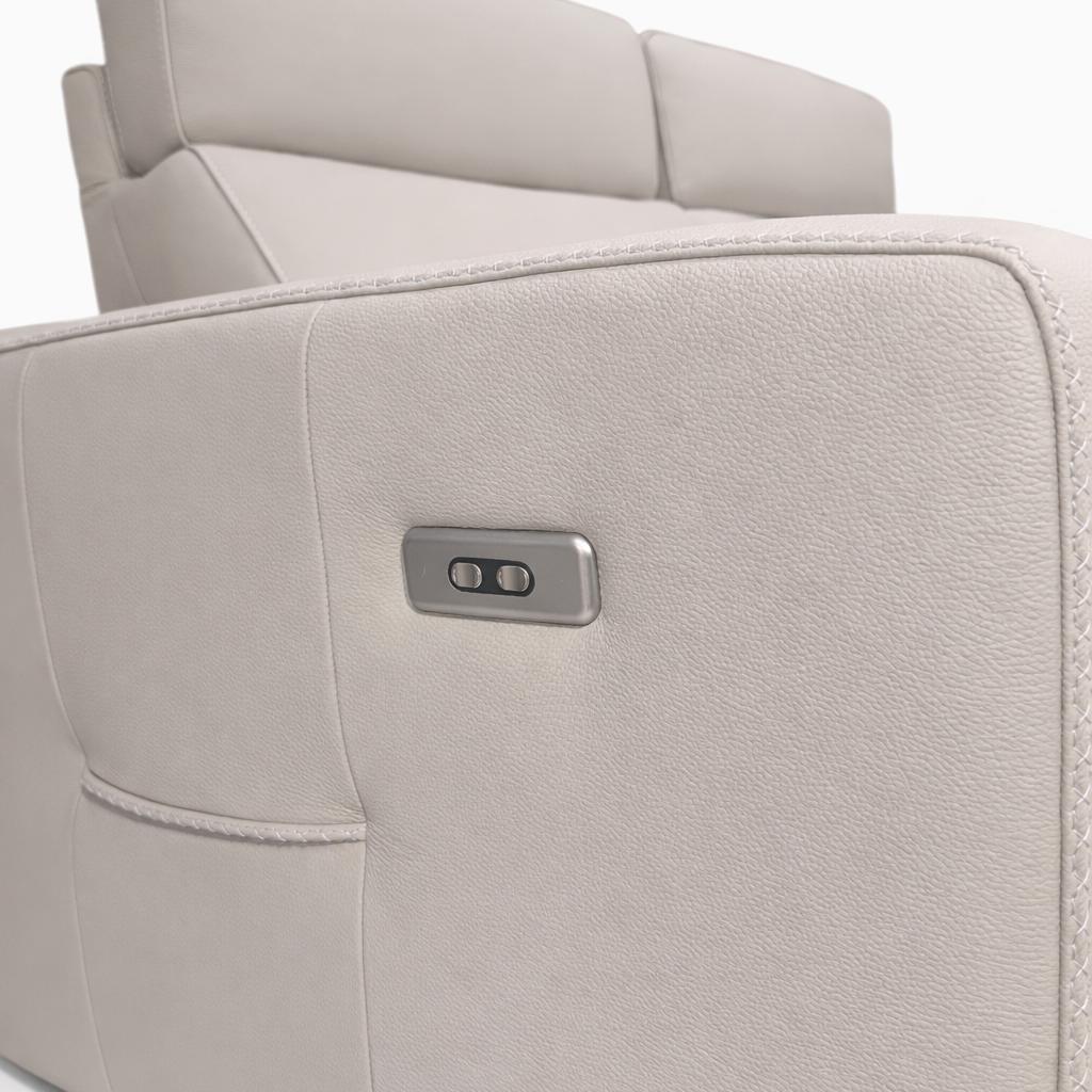 Close-up of a cream leather sofa side featuring a metallic control panel with two buttons and a side pocket.