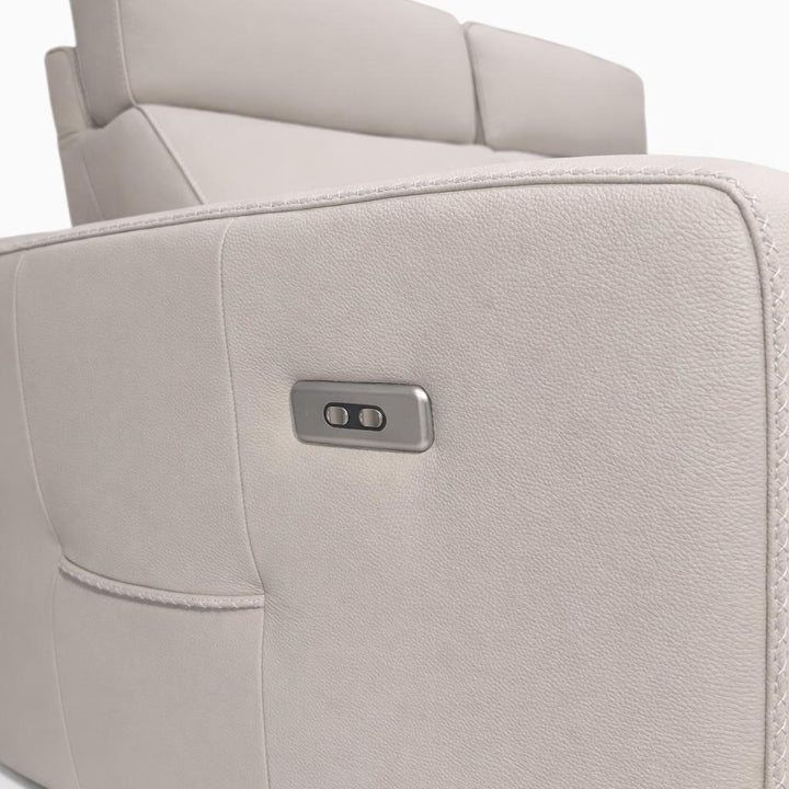 Close-up of a cream leather sofa side featuring a metallic control panel with two buttons and a side pocket.