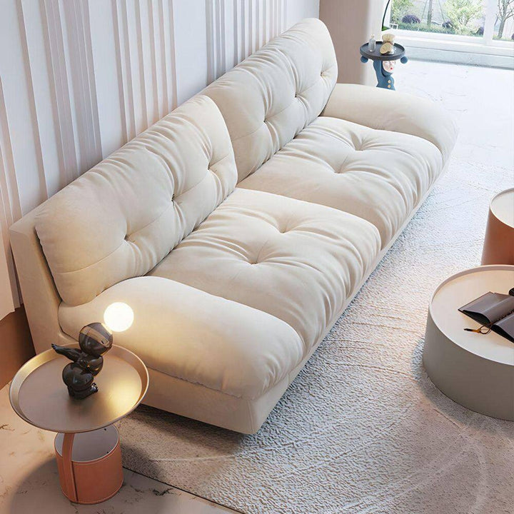 A modern living room scene features a cream-colored, button-tufted sofa, round side tables, and a window in the background.