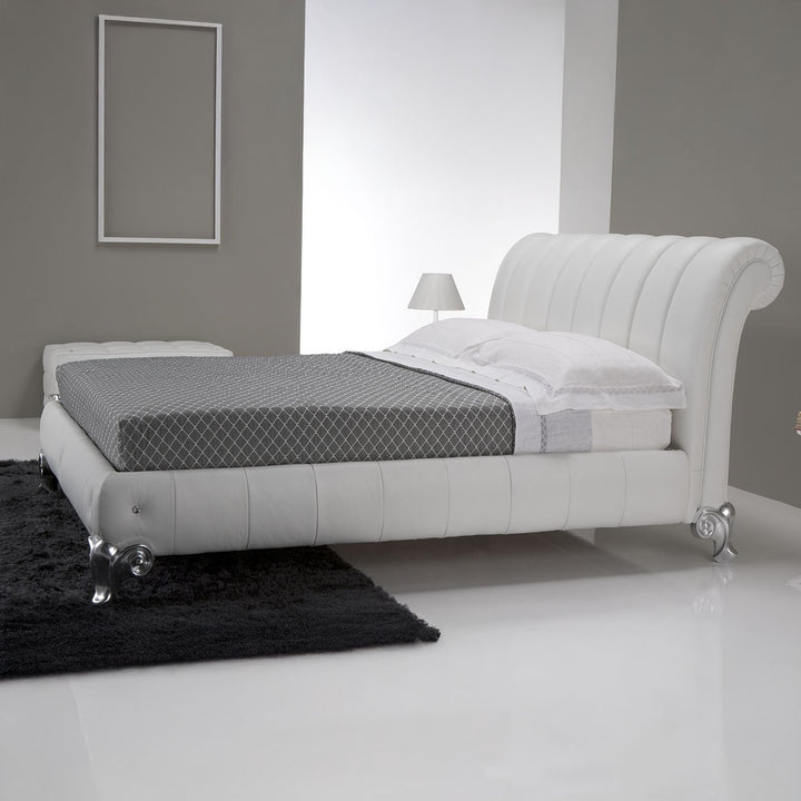 A white leather bed with a tufted headboard, a grey patterned blanket, and decorative feet, set in a modern bedroom with grey walls and a white floor.