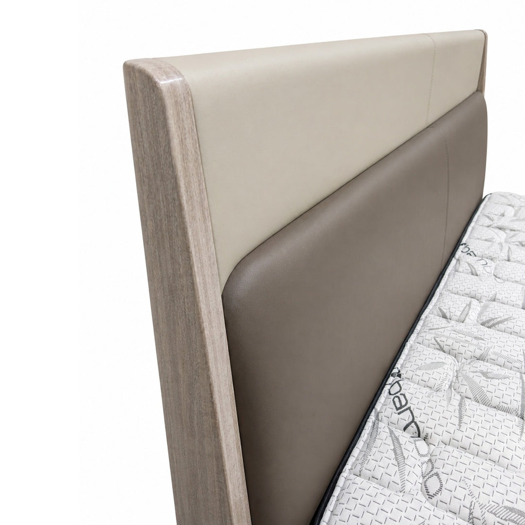 Angled view of a two-tone upholstered headboard with cream and taupe panels and a light wood side frame next to a mattress.