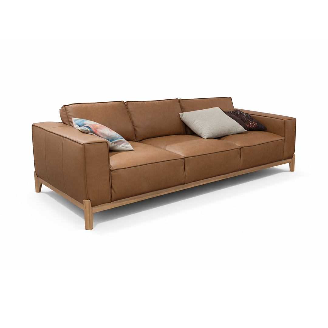 Angled view of a cognac leather 3-seater sofa with light wood legs and three decorative throw pillows.