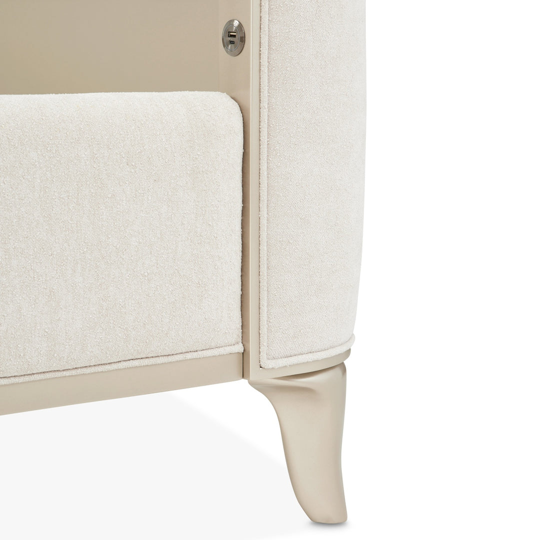 Close-up of a furniture piece, possibly an armchair, with a textured white fabric and light-colored wooden frame on a white background.