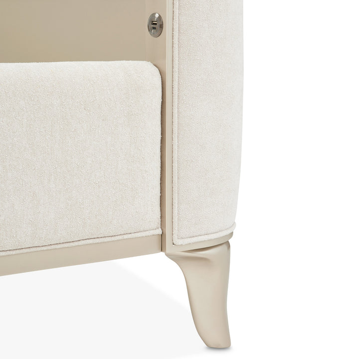 Close-up of a furniture piece, possibly an armchair, with a textured white fabric and light-colored wooden frame on a white background.