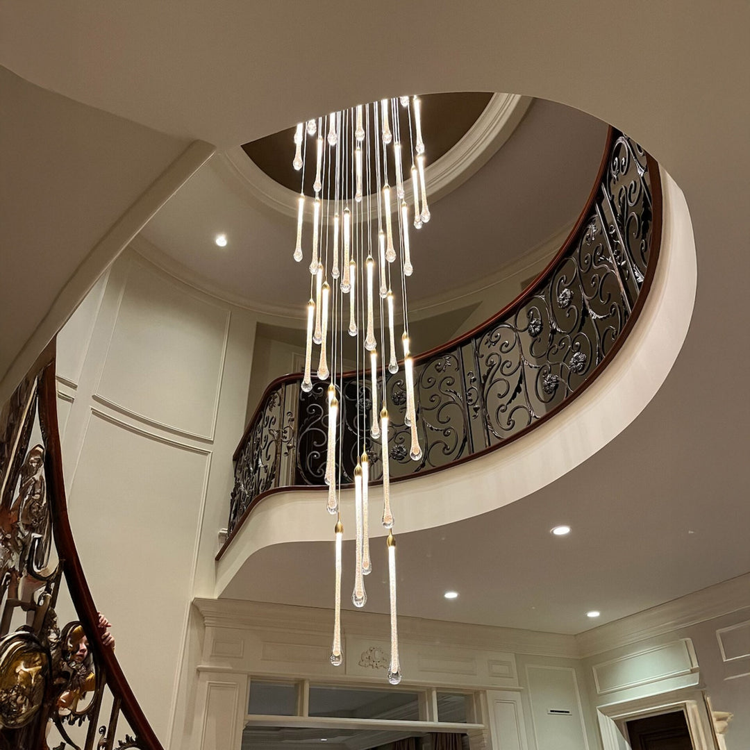 Image of a modern raindrop chandelier hanging in a luxurious two-story foyer with a curved staircase and wrought iron railing.
