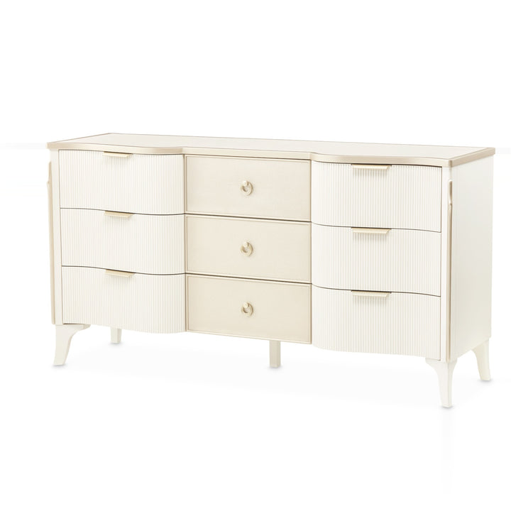 A white, long dresser with nine drawers is shown against a white background. The drawers have two different designs, vertical ribbed texture, and a smooth surface with round pulls. The top edge of the dresser has a gold trim.