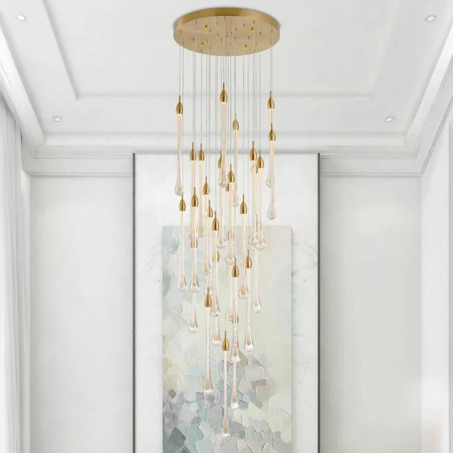 A gold chandelier with clear glass droplets hangs in a room with white walls and trim above an abstract painting.