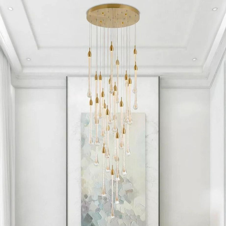 A gold chandelier with clear glass droplets hangs in a room with white walls and trim above an abstract painting.