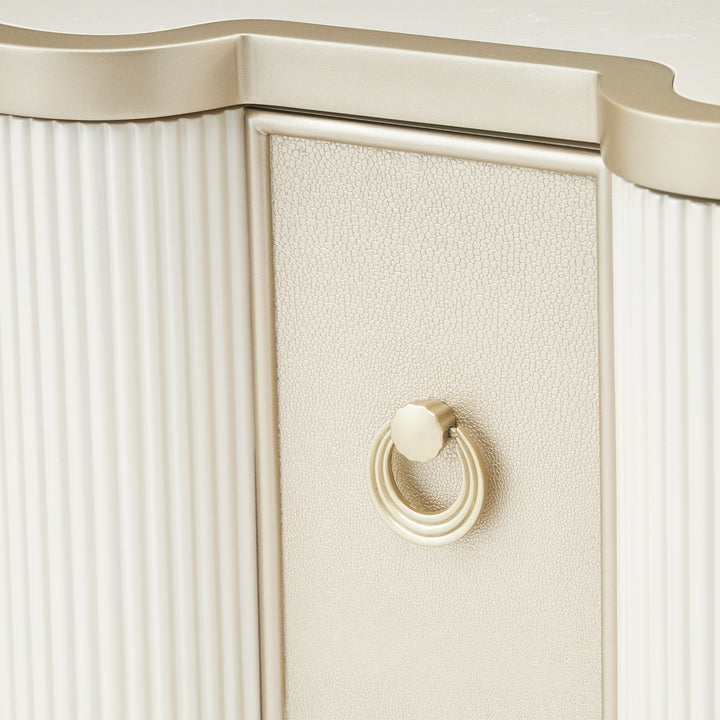 Close-up of a furniture piece featuring a textured cream drawer front with a round ring handle, accented by fluted paneling and a metallic trim.