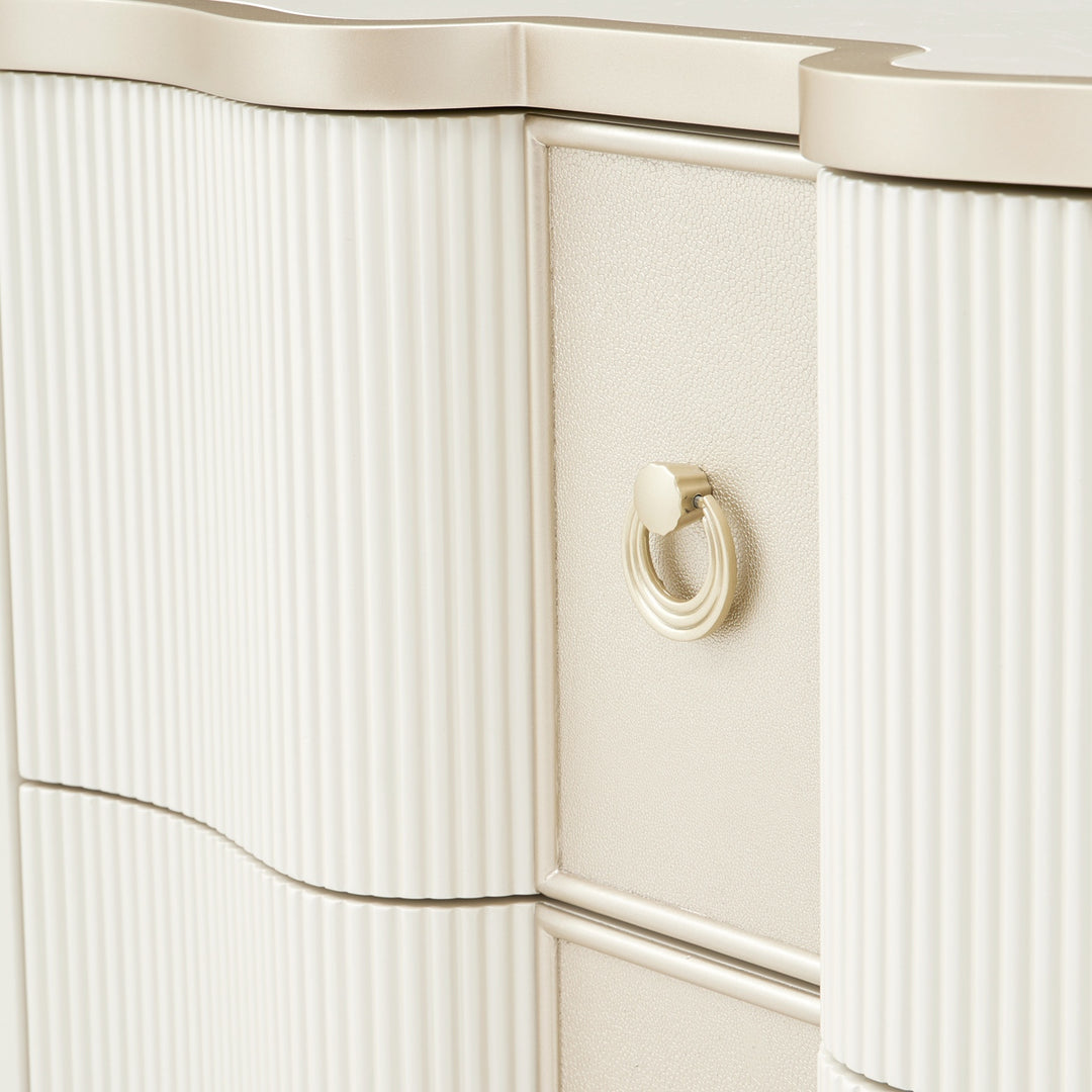 Close-up shot showcasing the material details of a white and gold dresser, including textured drawer fronts and metallic ring pulls.