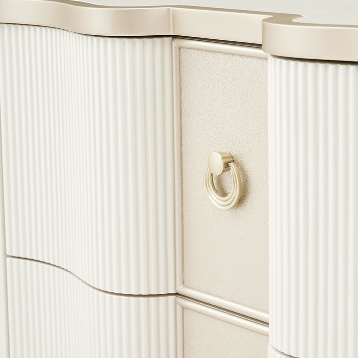 Close-up shot showcasing the material details of a white and gold dresser, including textured drawer fronts and metallic ring pulls.