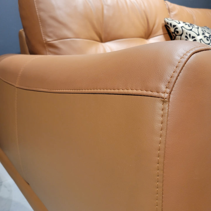 Close-up view of a caramel-colored leather sofa, showing the stitching and texture of the material.