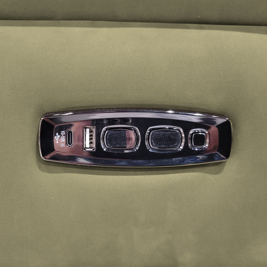 Close-up of a furniture control panel with USB ports and buttons, set against a green fabric background.