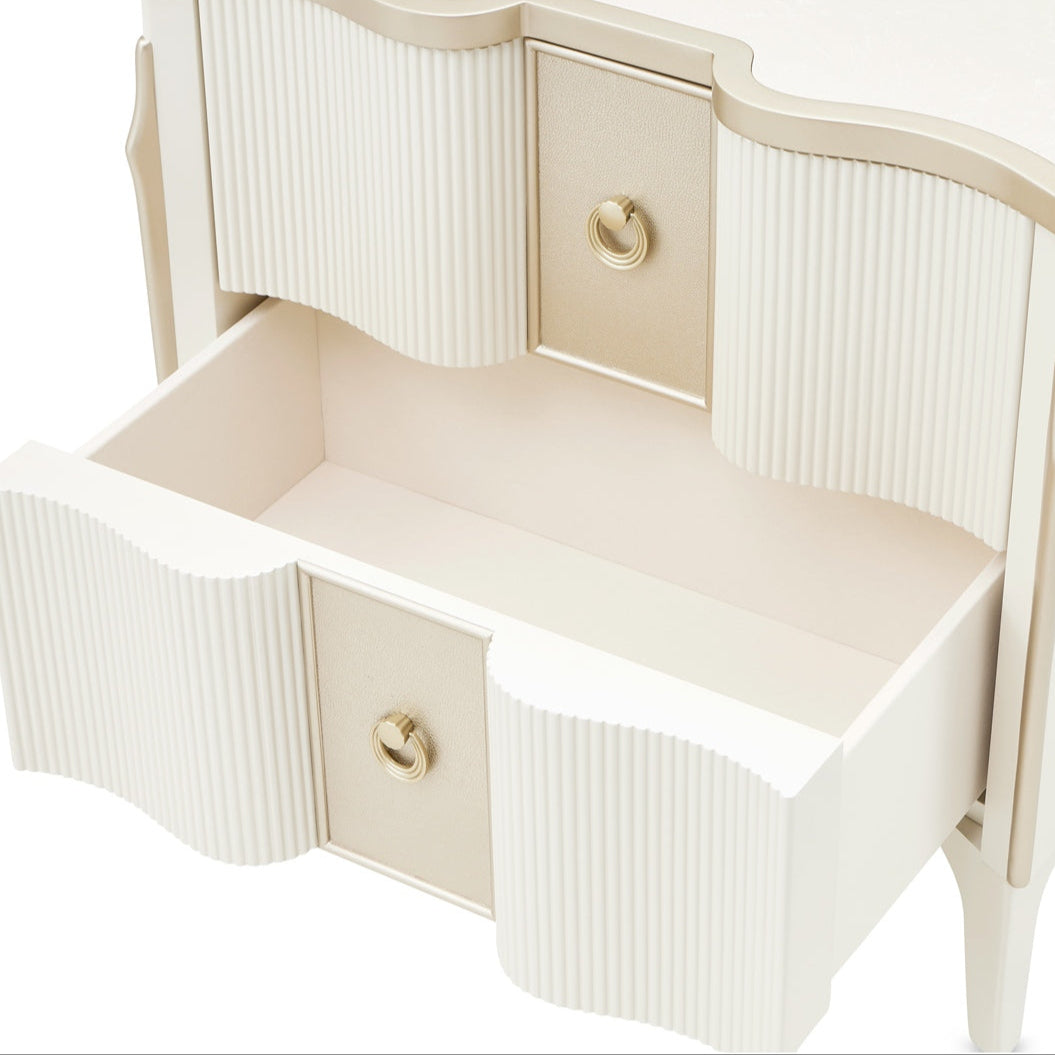 A white nightstand with gold accents and two drawers, one of which is open, set against a white background.
