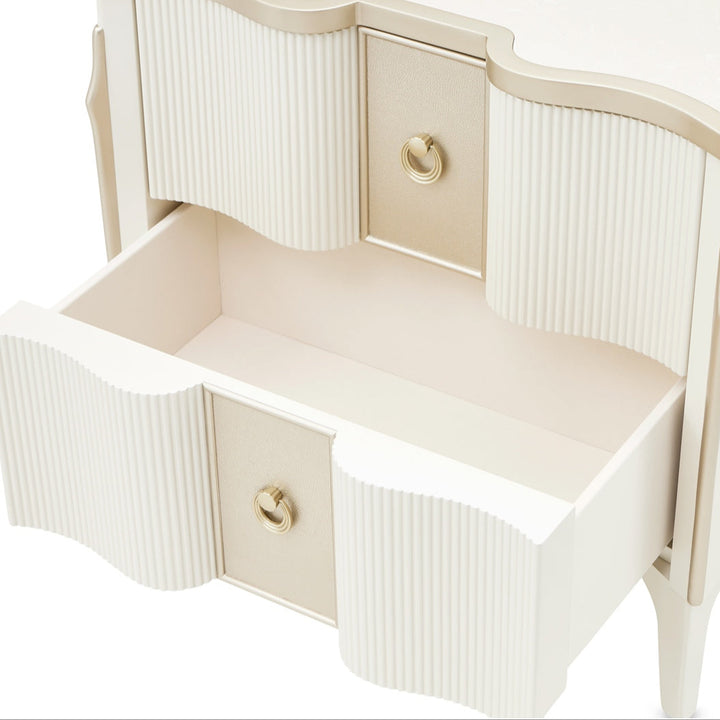 A white nightstand with gold accents and two drawers, one of which is open, set against a white background.