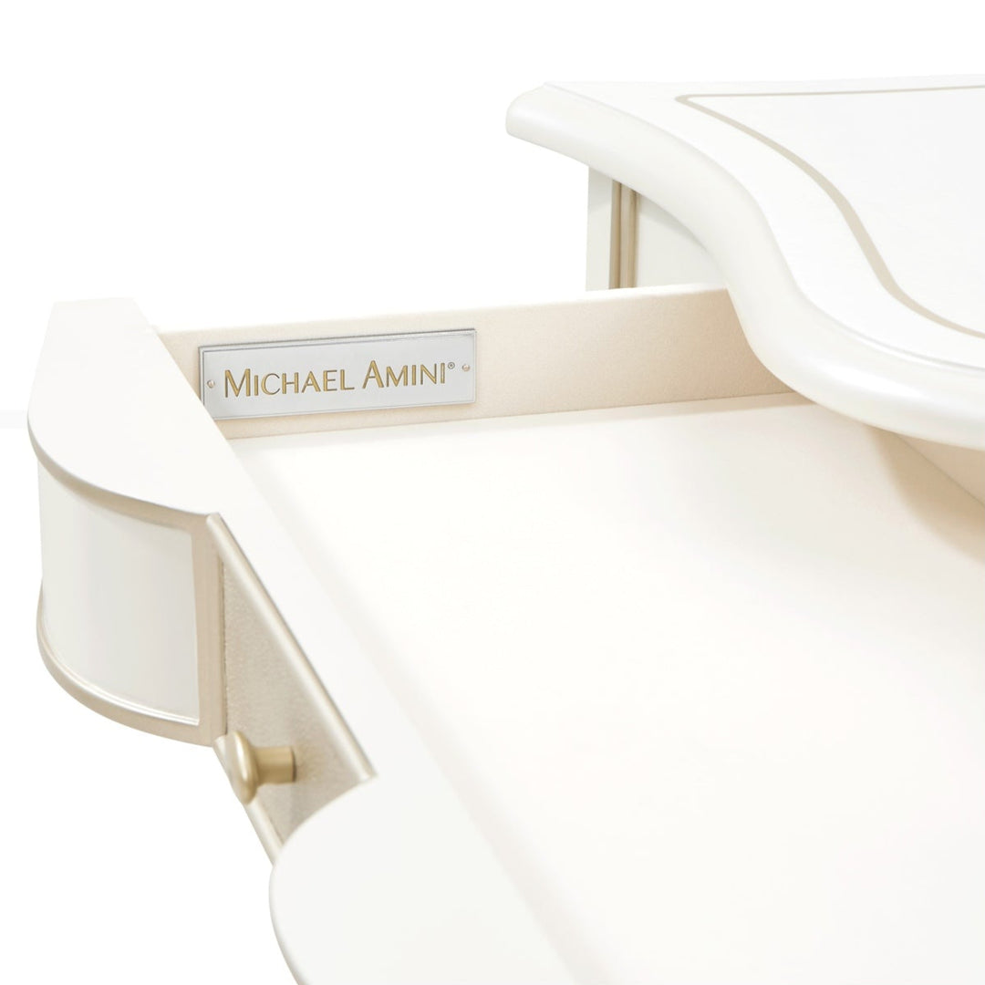 Close-up shot of a white furniture piece, possibly a desk or vanity, against a white background, showcasing the 'Michael Amini' brand plaque and drawer details.