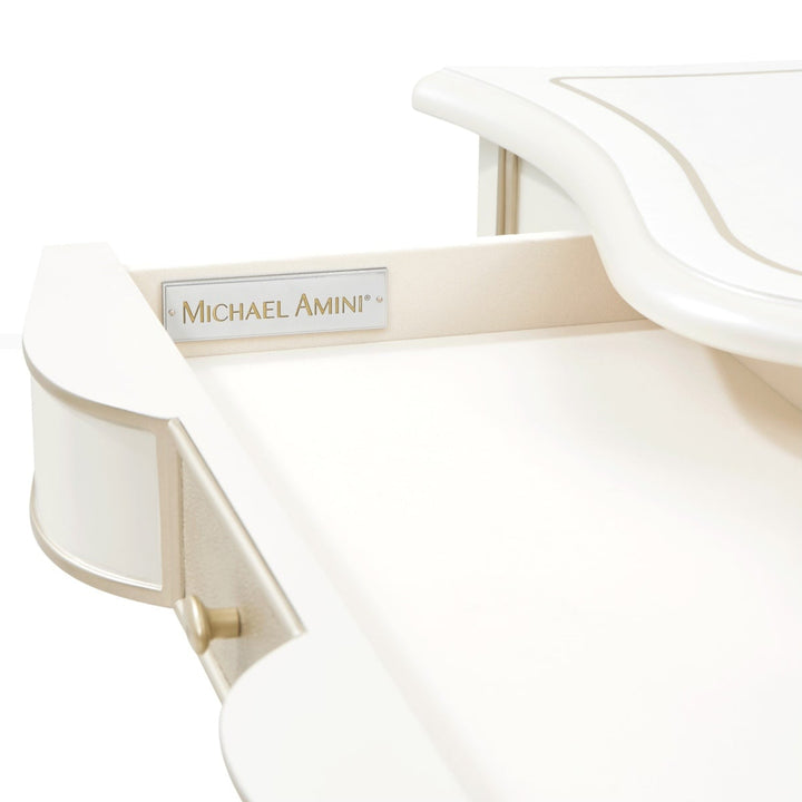 Close-up shot of a white furniture piece, possibly a desk or vanity, against a white background, showcasing the 'Michael Amini' brand plaque and drawer details.