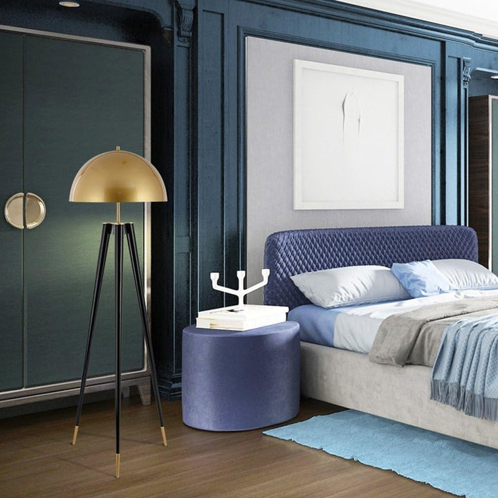 A bedroom scene with dark blue and gold accents, featuring a bed, storage unit, side table, and tripod lamp.