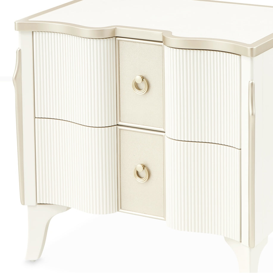 Close-up of a white and gold nightstand with two drawers and ring pulls on a white background.