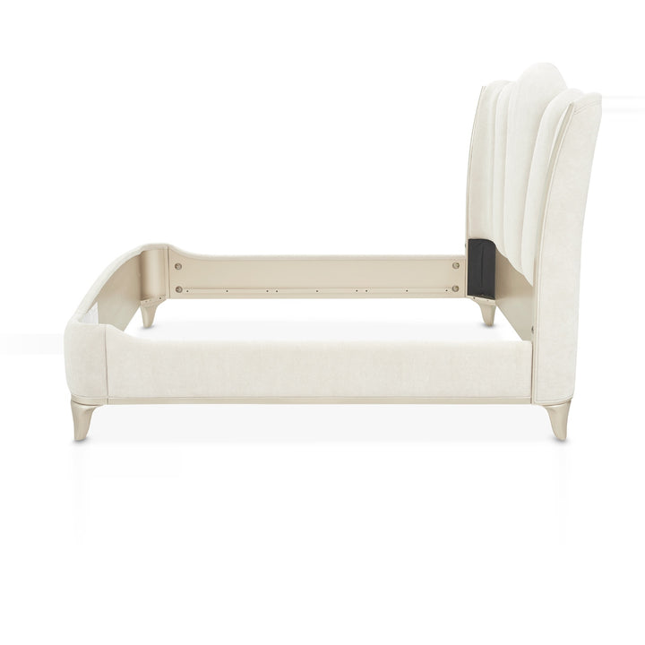 Side view of a luxurious white upholstered bed frame with a tall, curved headboard and silver legs, set against a plain white background.