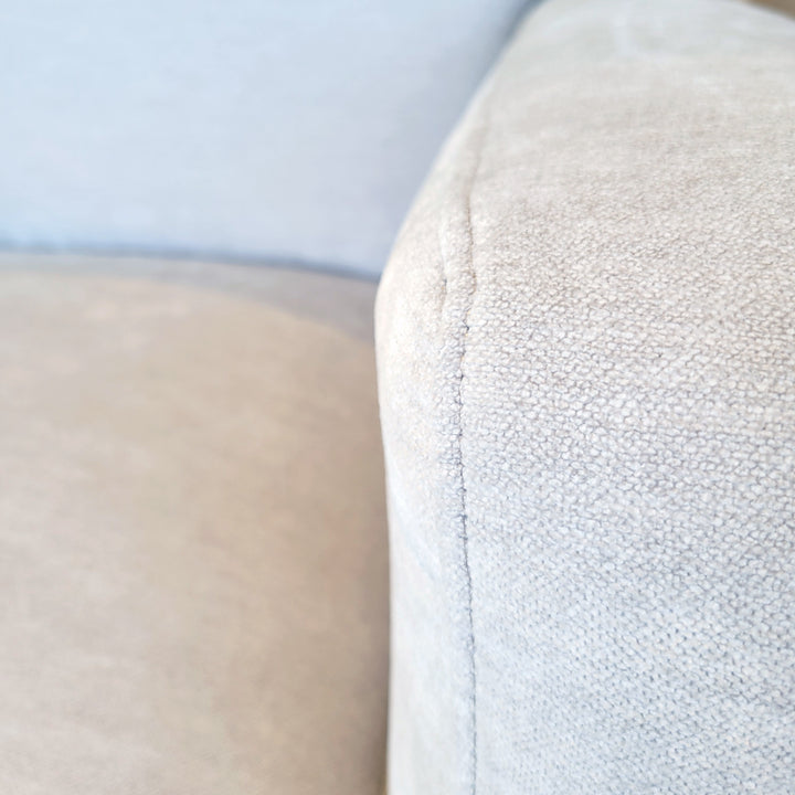 Close-up shot of a light gray upholstered furniture corner, highlighting the fabric texture and stitching.