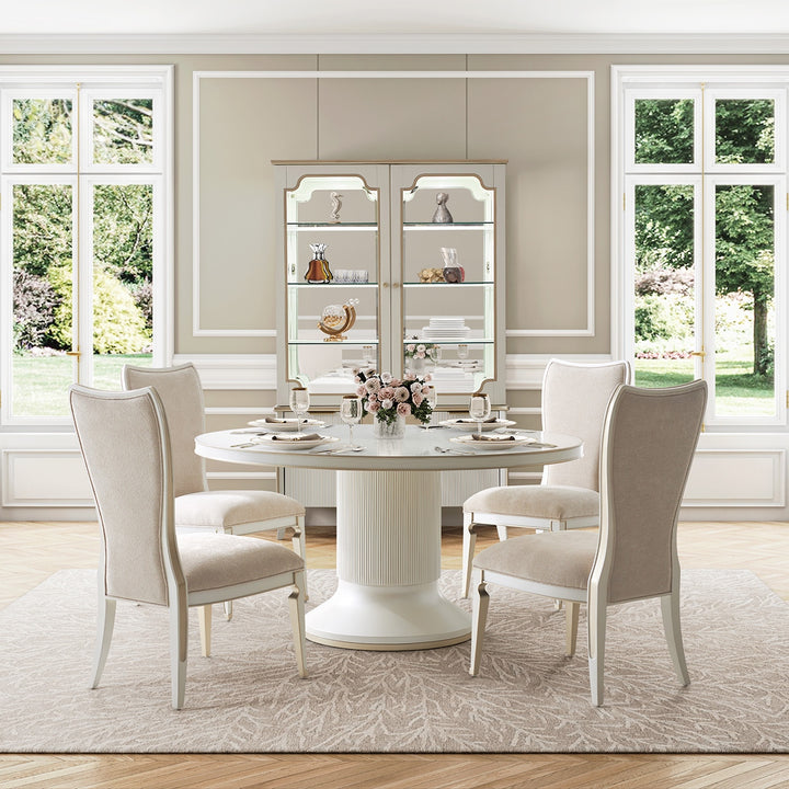 Dining room setting featuring a round table, four chairs, a cabinet with glass doors, and three large windows with a view to the outdoors.
