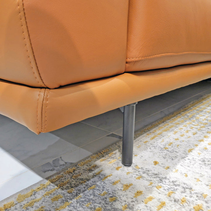 Close-up shot of a tan leather sofa with metal legs on a patterned rug in a room setting.