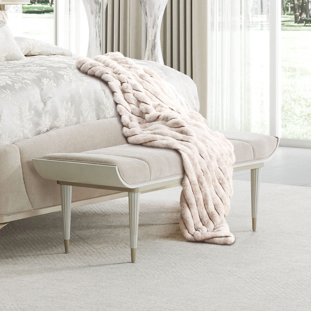 Bedroom scene featuring a light beige bench with a fur throw at the foot of a bed.