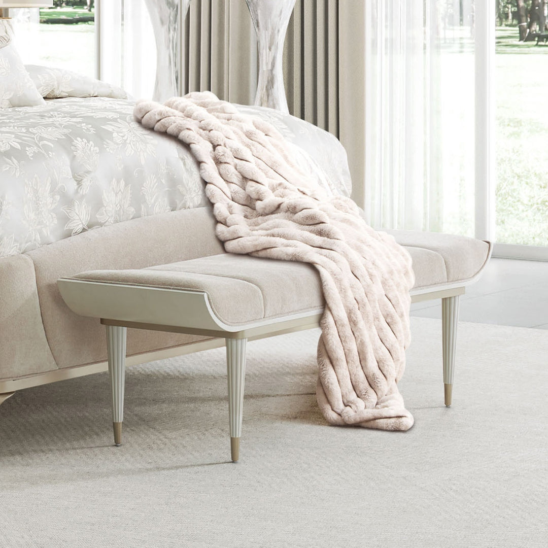 Bedroom scene featuring a light beige bench with a fur throw at the foot of a bed.
