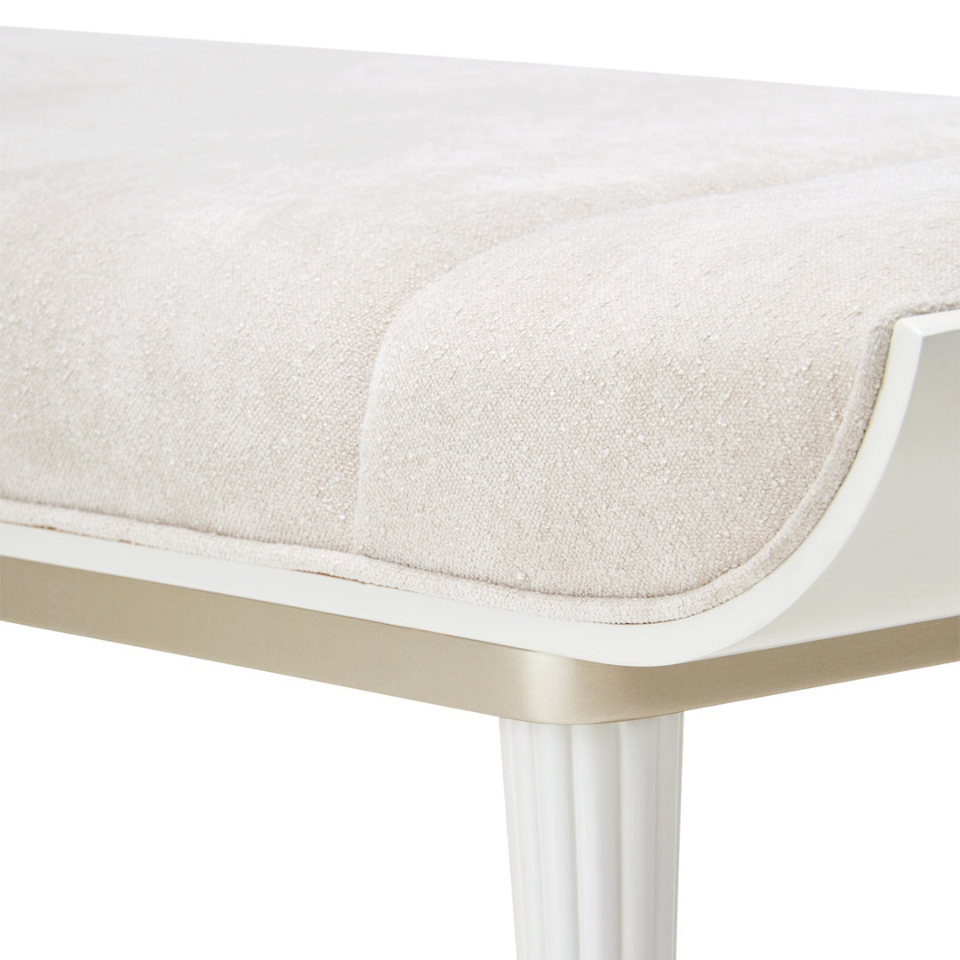 Close-up of a white upholstered bench with fluted legs on a white background.