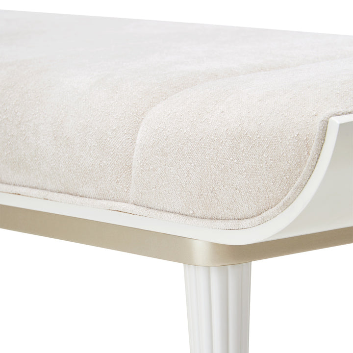 Close-up of a white upholstered bench with fluted legs on a white background.