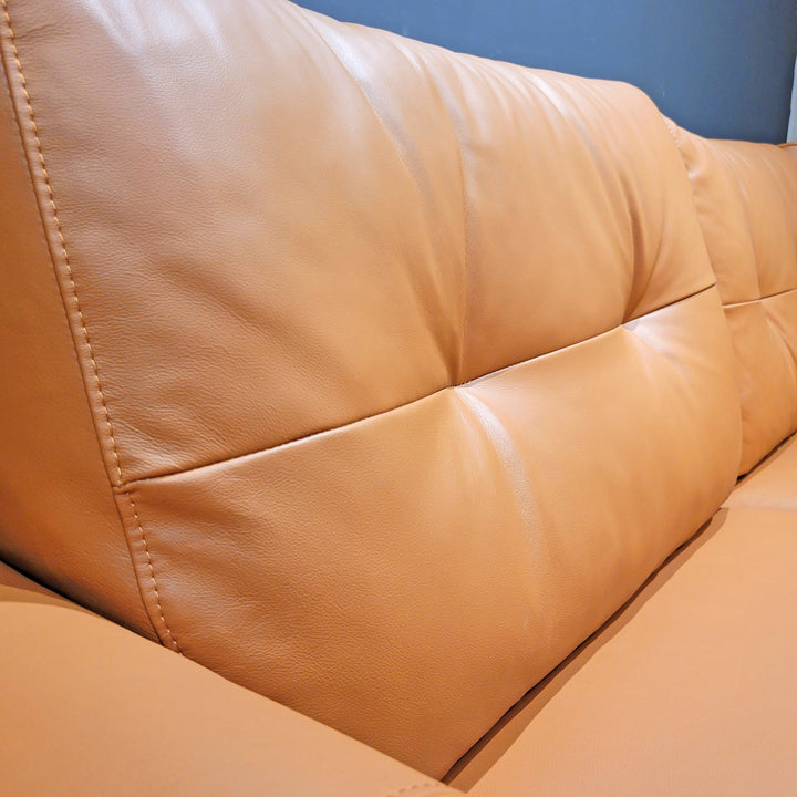 Close-up of a tan leather couch cushion, showing texture and stitching details.