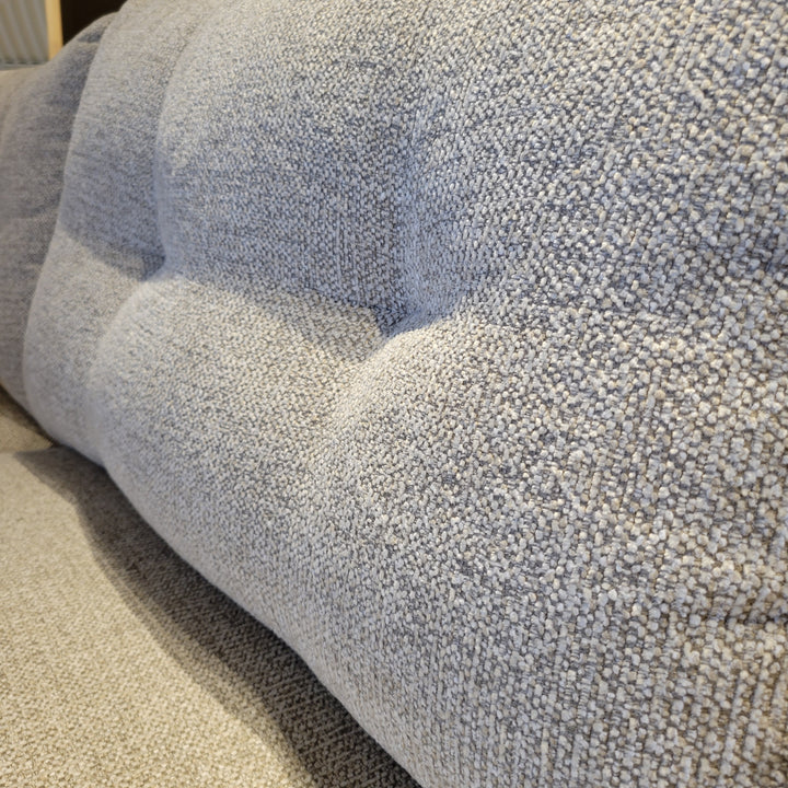 Close-up shot of a grey textured fabric on a sofa with tufted cushions.