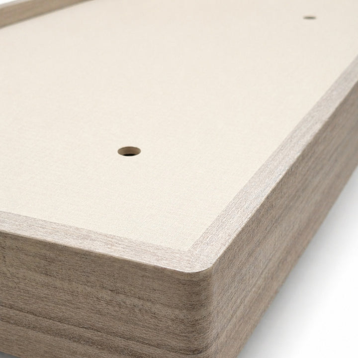 Close-up corner view of a light wood grain headboard featuring a cream fabric front panel and small circular holes.